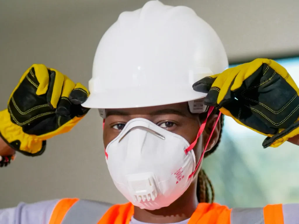 Pekerja konstruksi menggunakan alat pelindung diri lengkap termasuk helm, masker N95, dan sarung tangan